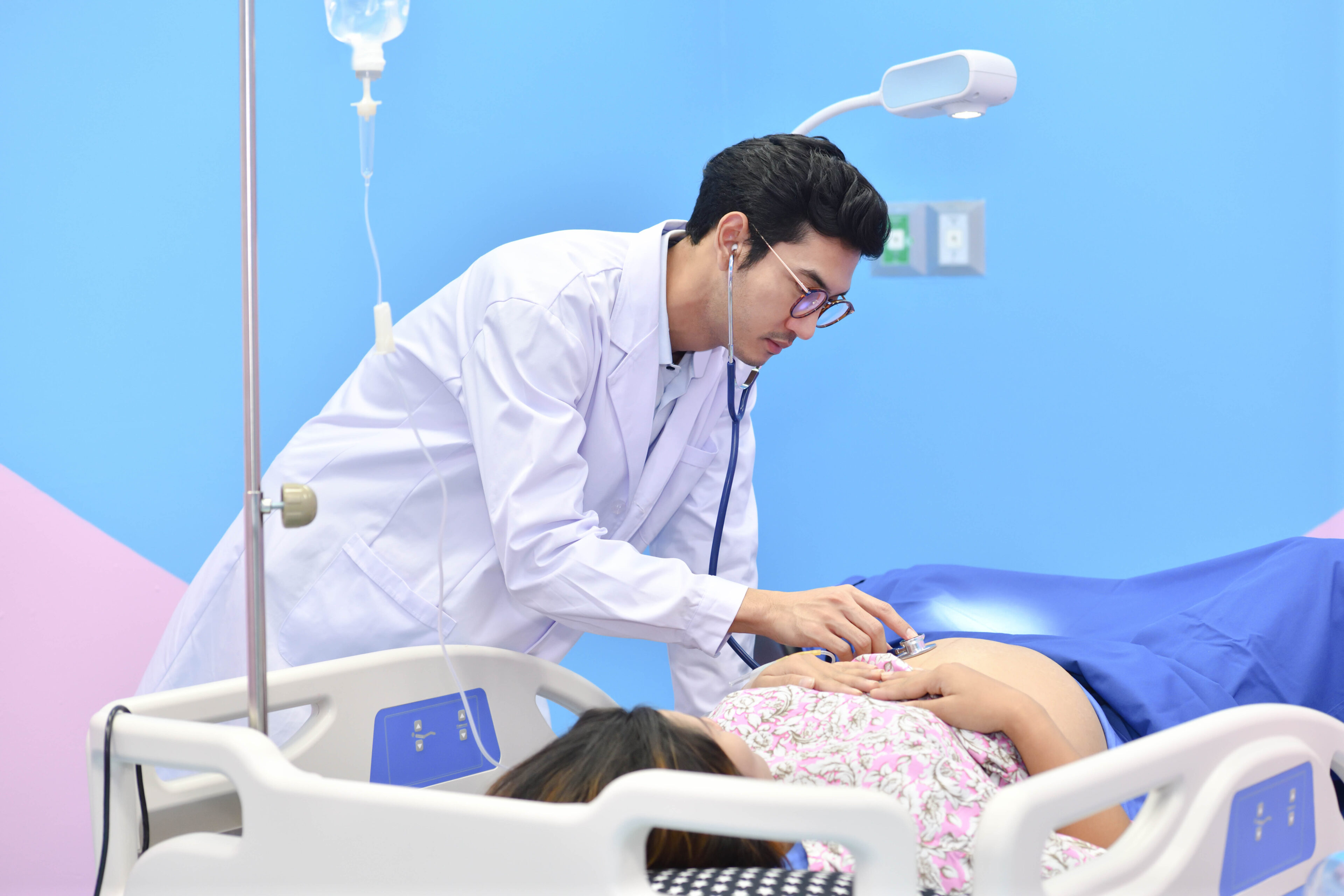 Asian doctor examining pregnant woman with stethoscope at maternity ward