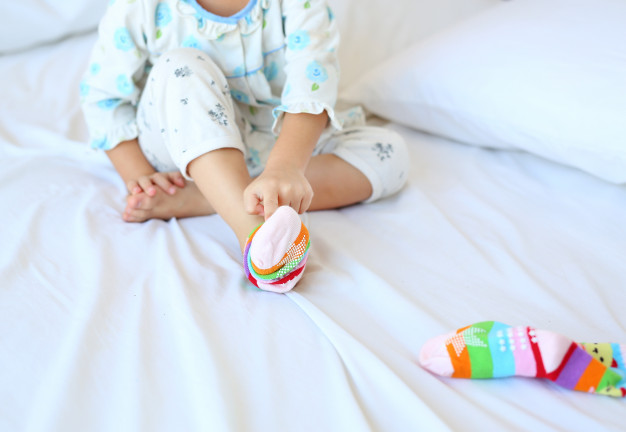 lovely-little-asian-girl-trying-put-socks-bed_38678-3806